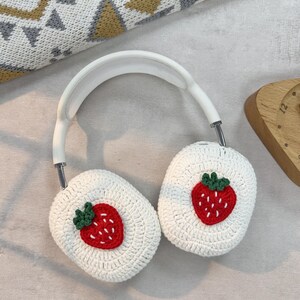 May include: White crocheted headphone covers with a red and green embroidered strawberry design.