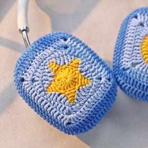 Puede incluir: Un par de fundas para auriculares de ganchillo azul y amarillo. Las fundas est&aacute;n hechas con un patr&oacute;n de cuadrado de la abuela y tienen una estrella amarilla en el centro.