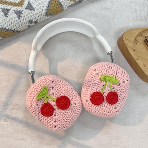 K&ouml;nnte beinhalten: Rosa gestrickte Kopfh&ouml;rerbez&uuml;ge mit einem Kirschendesign. Die Bez&uuml;ge sind aus weichem Garn gefertigt und haben ein wei&szlig;es Kopfband.