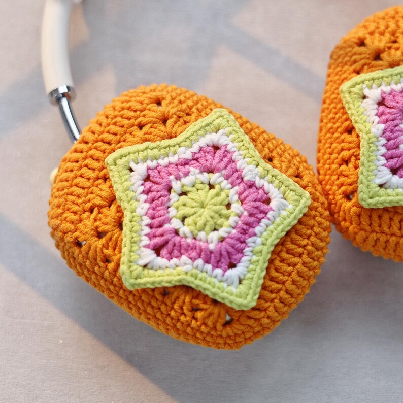 May include: A pair of orange crocheted headphone covers with a star-shaped design in pink, green, and white.