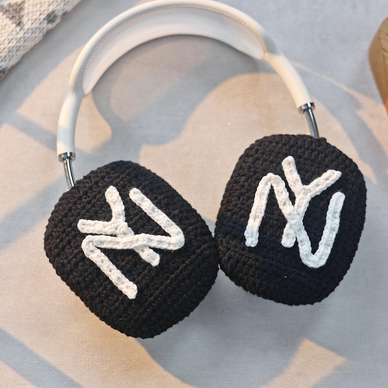 May include: Black crocheted earmuffs with white "NY" lettering. The earmuffs are attached to a white headband.