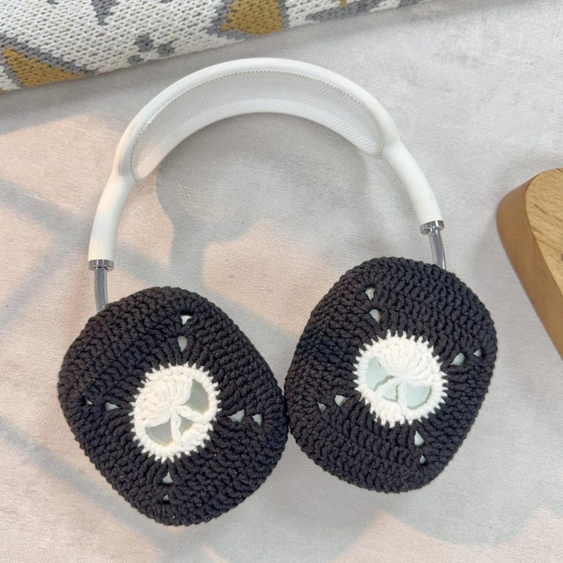 May include: Black and white crocheted ear covers for headphones. The ear covers have a white crocheted circle in the center.