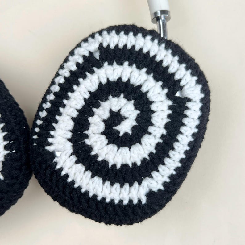 Pode incluir: Capas de fone de ouvido de croch&ecirc; em preto e branco. As capas apresentam um padr&atilde;o em espiral de listras pretas e brancas alternadas. Os fones de ouvido t&ecirc;m uma faixa branca e detalhes prateados.