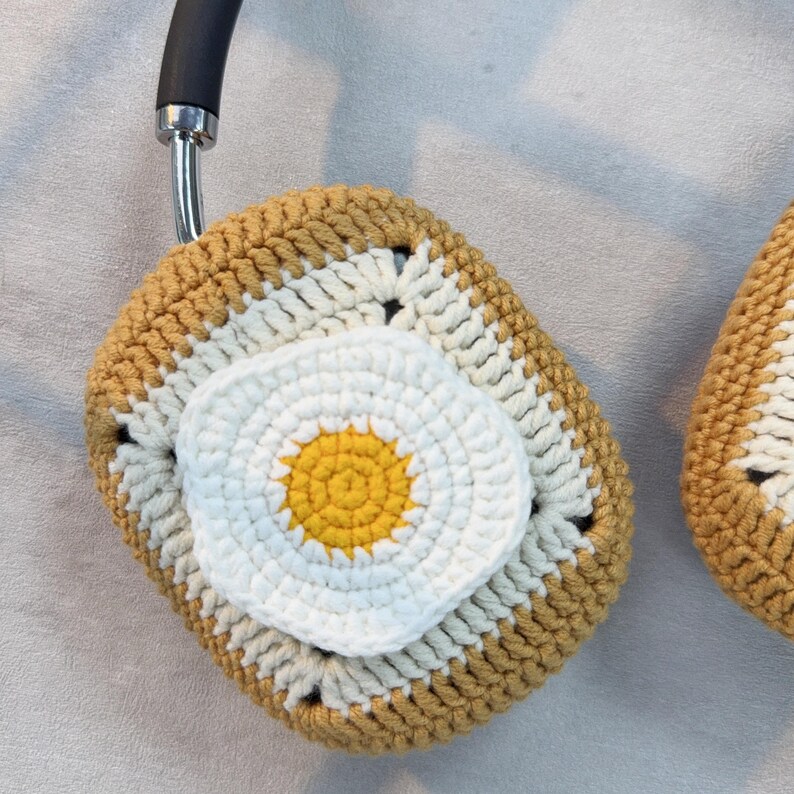 May include: Crocheted headphone covers in the shape of a fried egg. The yolk is yellow and the white is white. The cover is brown and white.