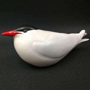 May include: A white ceramic bird figurine with a black head and red beak. The bird is in a flying pose with its wings spread out.