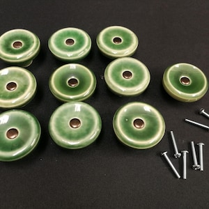 Puede incluir: Diez pomos redondos de cerámica para armarios con un esmalte verde brillante que se aclara hacia el centro. Cada pomo presenta un pequeño acento circular de color marrón oscuro en el medio. Se incluyen diez tornillos de metal plateado.