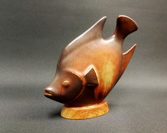 May include: A ceramic fish figurine with a brown and orange glaze. The fish is standing on a wooden base.