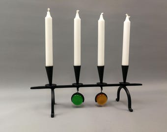 May include: A black metal candle holder with four white candles and two colored glass ornaments. The ornaments are green and orange.