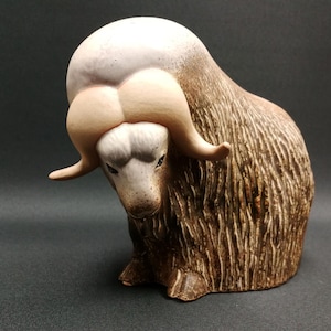 May include: A ceramic figurine of a musk ox with a white head and brown body. The ox is standing on all fours with its head lowered.