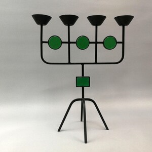 May include: A black metal candelabra with five candle holders and green accents. The candelabra has a tripod base.