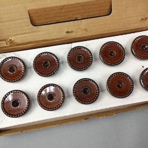 May include: Ten brown ceramic drawer pulls with a decorative border. The pulls are arranged in two rows of five.