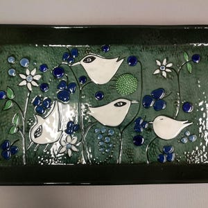 Puede incluir: Bandeja rectangular de cerámica con borde verde oscuro e interior verde azulado texturizado. La bandeja presenta pájaros blancos, bayas azules y flores blancas. El diseño es una ilustración estilizada con temática de la naturaleza.