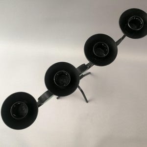 May include: Black metal candle holder with four candle cups. The holder has a decorative, branched design.