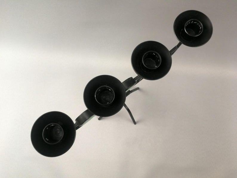 May include: Black metal candle holder with four candle cups. The holder has a decorative, branched design.