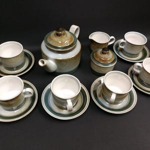 May include: A vintage tea set with a teapot, creamer, sugar bowl, and six cups with saucers. The set features a color palette of green, brown, and white. The teapot has a rounded shape with a lid. The cups and saucers have a matching design.