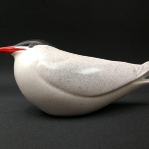 May include: A white ceramic bird sculpture with a black head and a red beak. The bird has a speckled, textured surface.