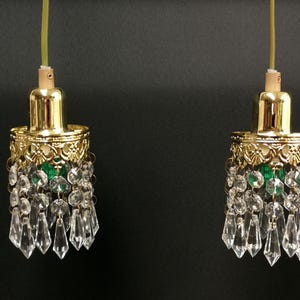 Pode incluir: Duas luminárias pendentes a condizer com tampas de metal dourado polido e detalhes em filigrana ornamentados. Cada luminária é adornada com múltiplos prismas e contas de vidro transparente, suspensas por um cabo de cor clara.