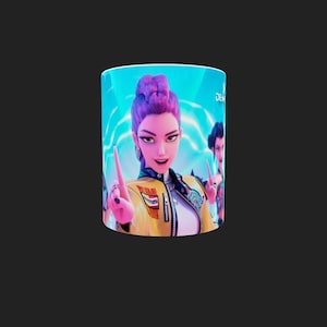 Op de afbeelding: Een witte keramische mok met een cartoonillustratie van een vrouw met paars haar en een gele jas. De mok heeft een blauwe achtergrond met andere personages op de achtergrond.