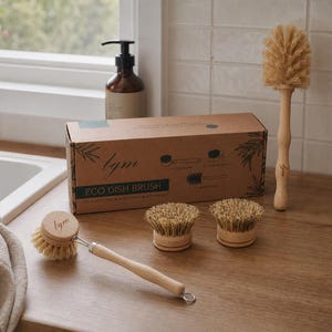 May include: A set of eco dish brushes featuring light wood handles and natural tan bristles. The set includes one long-handled brush, one brush with a short handle, and two round brush heads, all packaged in a brown cardboard box labeled Eco Dish Brush.