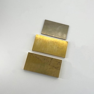 Può includere: Tre piastre metalliche rettangolari in varie tonalità di oro e argento. La piastra superiore è argentata, la piastra centrale è dorata e la piastra inferiore è di un oro più scuro. Tutte le piastre hanno un aspetto metallico spazzolato.