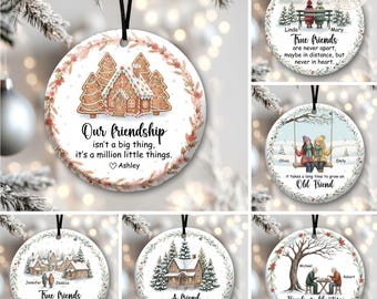 May include: A round white ceramic ornament featuring a gingerbread house illustration, a floral wreath border, and the text: Our friendship isn't a big thing, it's a million little things. Ashley. It hangs from a black ribbon for display.