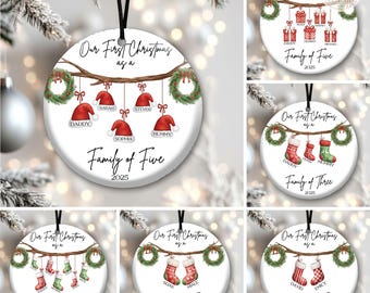 May include: A round white ceramic Christmas ornament featuring a brown tree branch with hanging green wreaths and red Santa hats or stockings. The text reads Our First Christmas as a Family of Five 2025 with personalized names below each item.