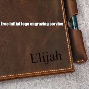 May include: A brown leather journal with a pen holder and the name "Elijah" engraved on the front. The journal has a stitched edge and a free initial logo engraving service is offered.