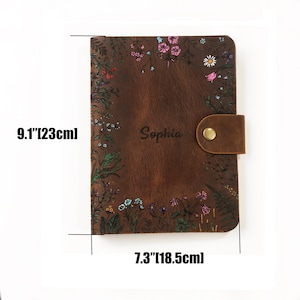 May include: A brown leather journal featuring a floral print border and the name Sophia engraved in the center. The journal includes a brass snap closure and measures 9.1 inches by 7.3 inches as indicated by the text on the image.