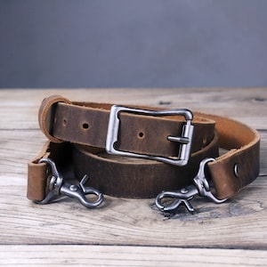 May include: A brown leather camera strap with a silver buckle and two silver clasps.