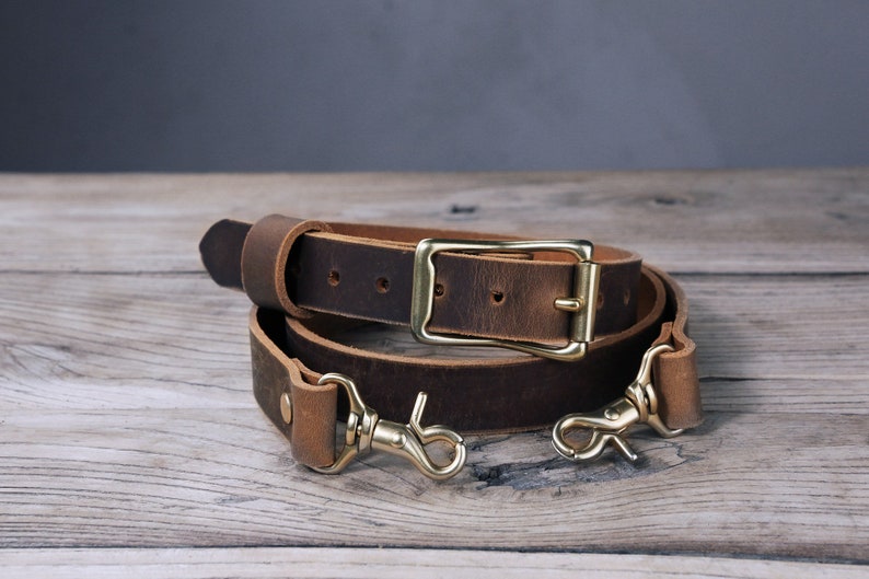May include: A brown leather camera strap with a brass buckle and two brass hooks.