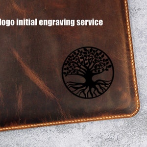 May include: A brown leather notebook with a stitched edge and a tree of life design engraved on the front. The text "Free logo initial engraving service" is printed above the design.