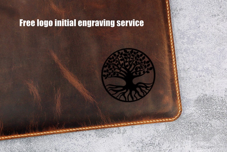 May include: A brown leather notebook with a stitched edge and a tree of life design engraved on the front. The text "Free logo initial engraving service" is printed above the design.