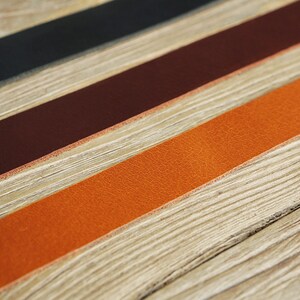 May include: Three leather strips in black, brown, and orange, laid out on a wooden surface.