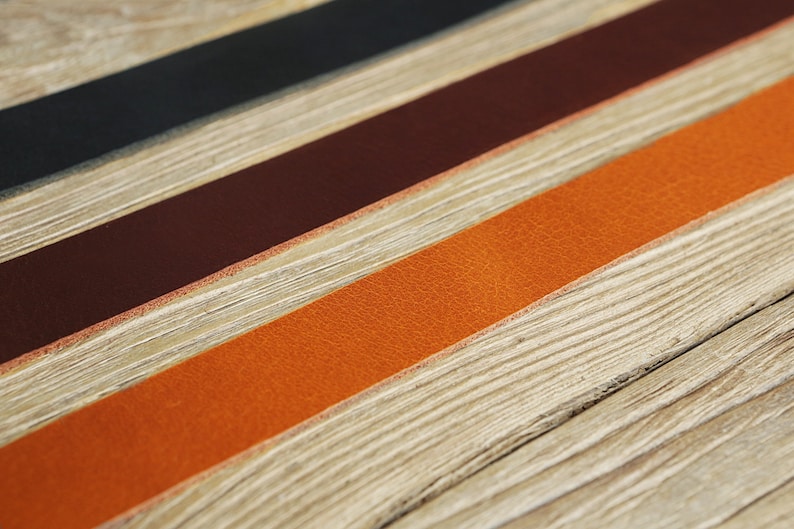 May include: Three leather strips in black, brown, and orange, laid out on a wooden surface.