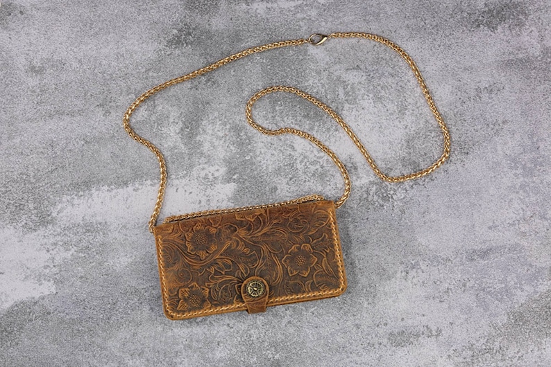 May include: A brown leather purse with a floral embossed design and a gold chain strap.