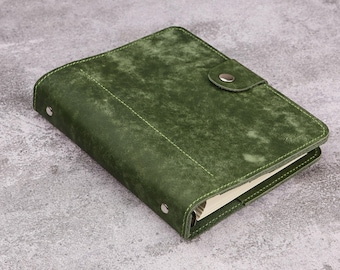 Puede incluir: Un cuaderno rectangular con una cubierta de color verde bosque texturizada y costuras visibles en los bordes. El cuaderno incluye un cierre de solapa asegurado con un botón de presión de metal plateado y dos remaches plateados en el lomo.