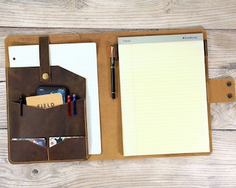 Könnte beinhalten: Ein braunes Lederportfolio mit einem Notizblock, einem Stift und einem Telefon im Inneren. Das Portfolio hat eine Klappe mit einem Druckknopfverschluss und mehrere Taschen zur Organisation. Der Notizblock ist liniert und trägt den Markennamen "EverReady" oben aufgedruckt.
