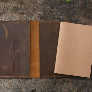 May include: A brown leather notebook cover with a tan leather flap and a blank notebook inside.