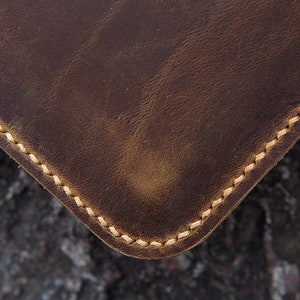 May include: Close-up of a brown leather item with a stitched edge. The stitching is a light brown color.