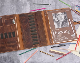 Może przedstawiać: Brązowe skórzane portfolio z szkicownikiem, uchwytami na ołówki i klapą z kieszenią. Szkicownik ma rysunek twarzy kobiety i napis "Strathmore Drawing" na okładce. Tekst poniżej brzmi "Drawing Paper & Sketch Pad, Papier de dessin, Cuaderno de dibujo, 24 sheets, feuilles, hojas".