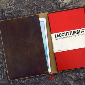 May include: A brown leather notebook cover with a red notebook inside. The notebook has the text "LEUCHTTURM1917" and "DETAILS MAKE ALL THE DIFFERENCE." on the front.