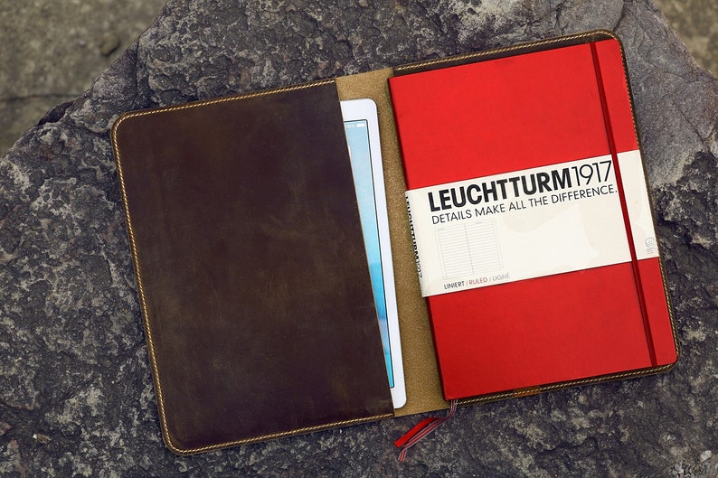 May include: A brown leather notebook cover with a red notebook inside. The notebook has the text "LEUCHTTURM1917" and "DETAILS MAKE ALL THE DIFFERENCE." on the front.