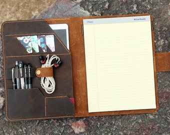 May include: A brown leather portfolio with a notepad, pens, and earbuds. The notepad has the words "Mead" and "EverReady" printed on it.