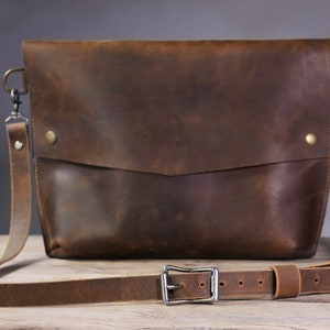 May include: A brown leather crossbody bag with a long adjustable strap and a silver buckle. The bag has a flap closure and a small pocket on the front.
