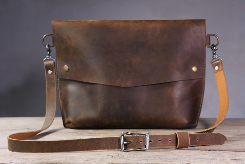 May include: A brown leather crossbody bag with a long adjustable strap and a silver buckle. The bag has a flap closure and a small pocket on the front.