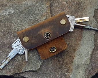 May include: A brown leather key holder with a snap closure and metal accents. The holder is open and several keys are sticking out.