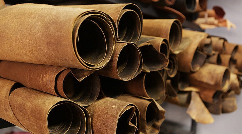 May include: Close-up of a stack of rolled brown leather hides. The hides are tightly rolled, revealing the edges of the leather. The color is a warm, earthy brown, with variations in tone. The image suggests a craft supply or material for leatherworking projects.
