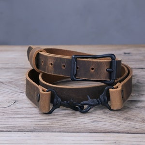May include: A brown leather camera strap with a black metal buckle and two black metal clips.