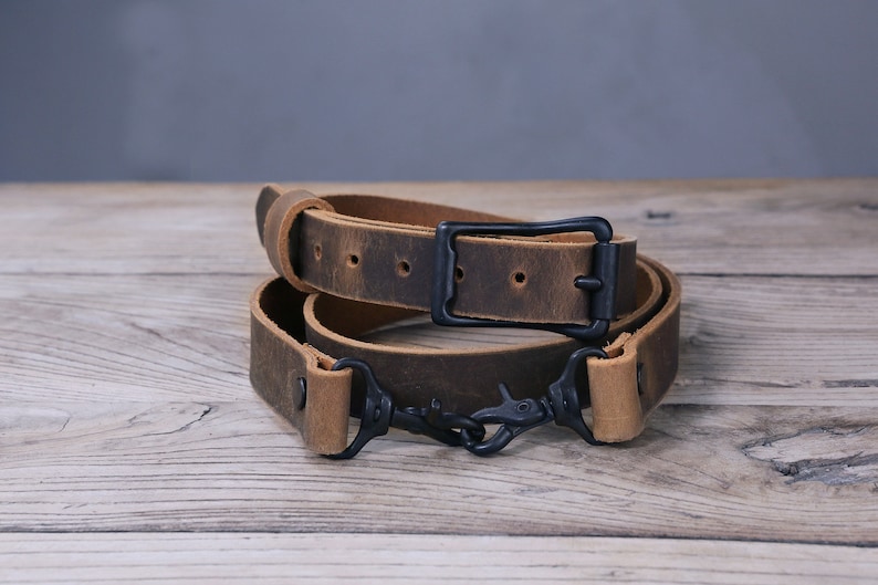 May include: A brown leather camera strap with a black metal buckle and two black metal clips.
