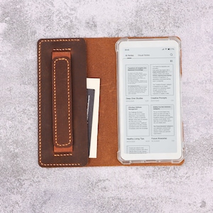 Puede incluir: Una funda de cuero marrón para lector de libros electrónicos con una funda de teléfono de plástico transparente que contiene un lector de libros electrónicos blanco. La funda tiene una ranura para tarjetas y una correa marrón. El lector de libros electrónicos muestra el texto "Al Notes" y "Visual Notes".